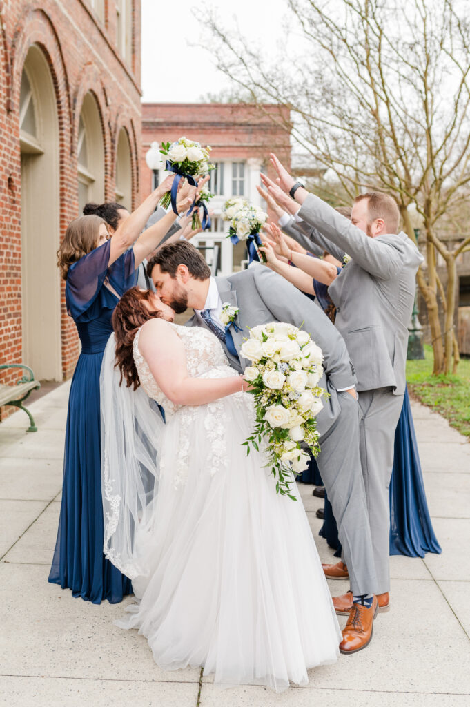 bride and groom kissing with wedding party behind them