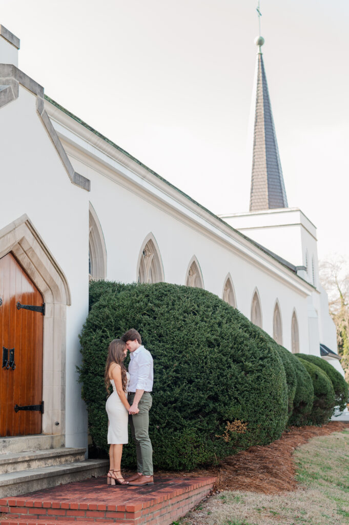 couple with foreheads together with church behind them