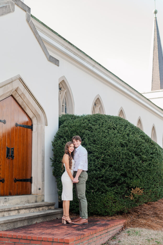 couple smiling at camera with church behind them