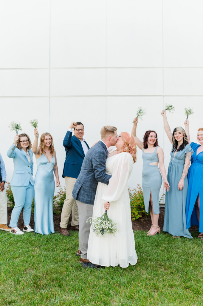 wedding party cheering while bride and groom kiss